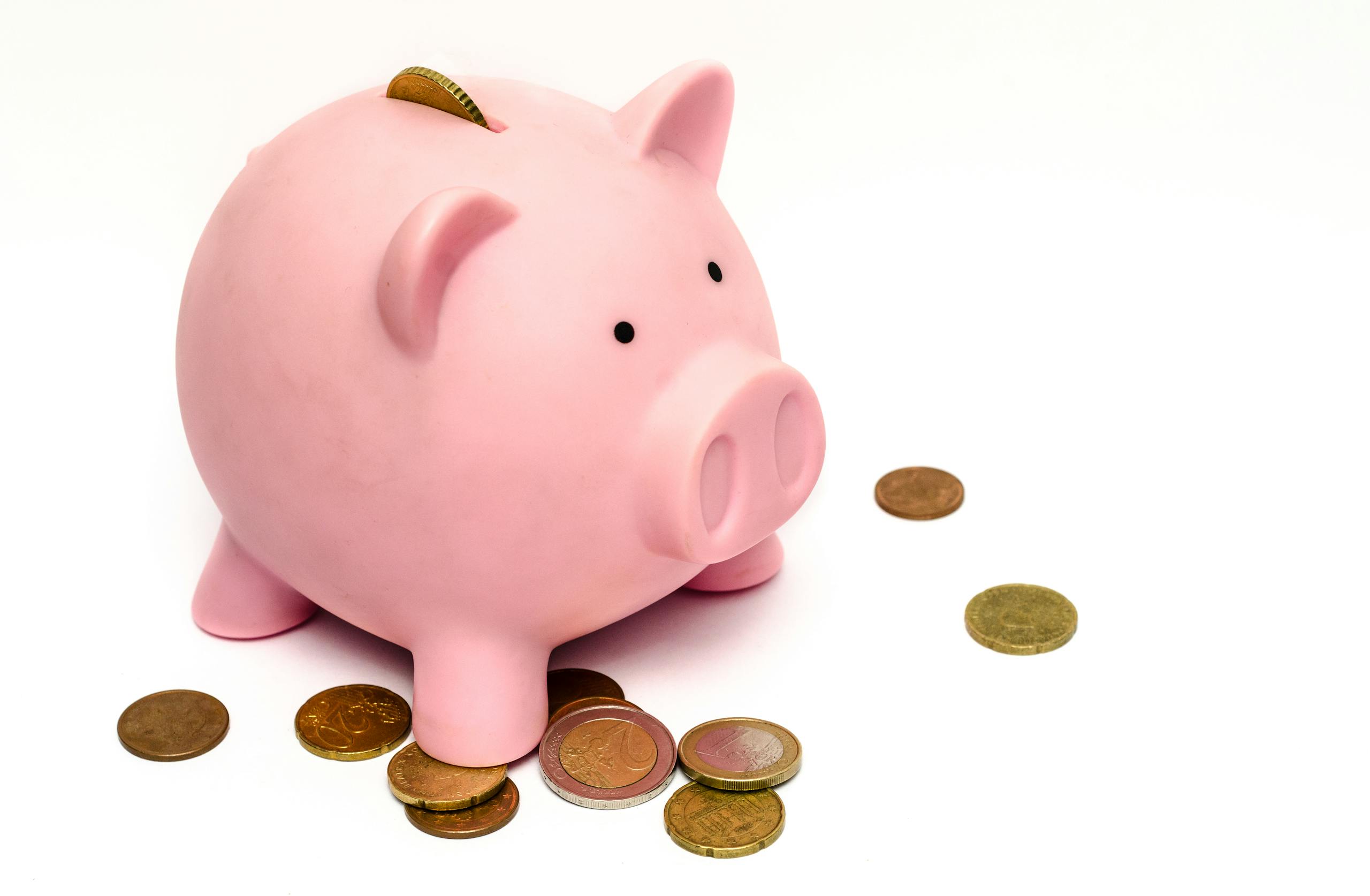 Close-up of a person's hand placing coins into a transparent piggy bank to save money.
