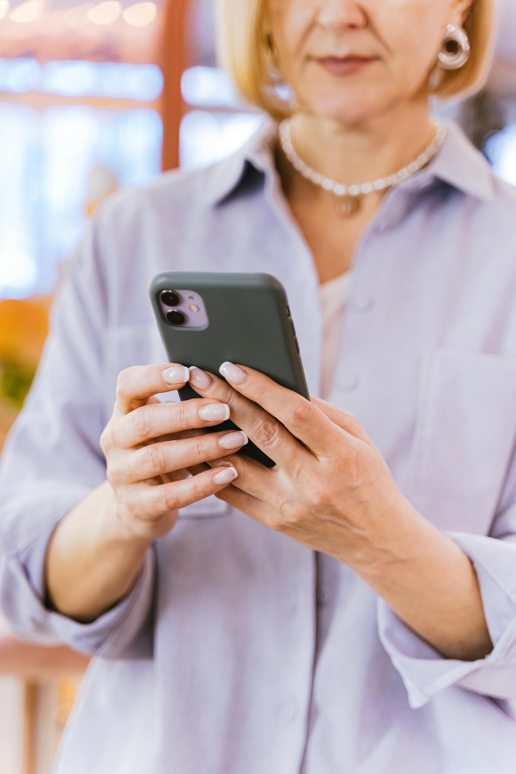 Close-up of a mature woman with short hair using a smartphone indoors, selective focus.
